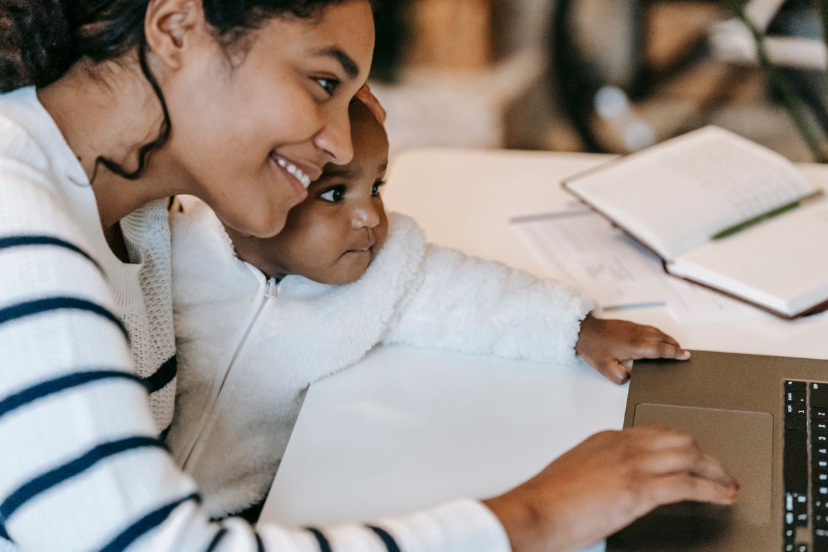 A young mother holding her baby while using a laptop